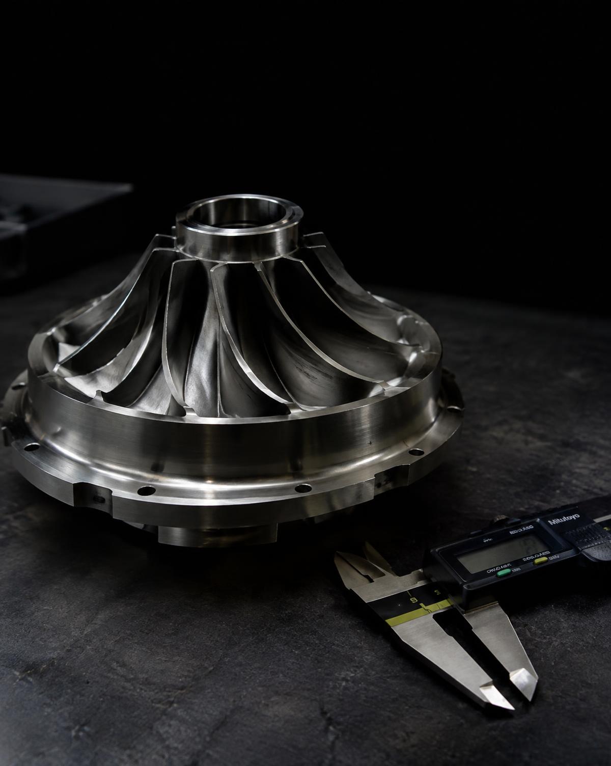 Precision-machined metal impeller and digital caliper on a dark workbench